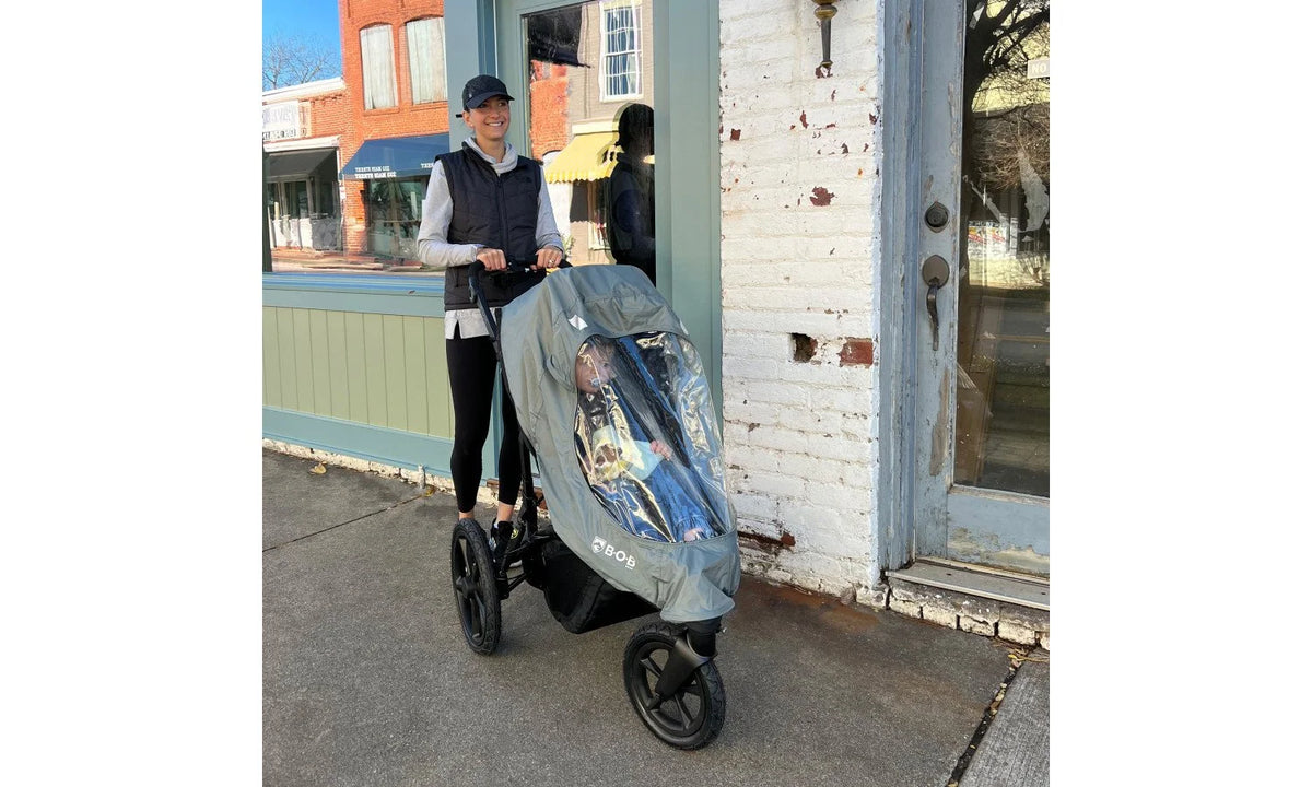 A woman pushing a jogging stroller with a rain cover.